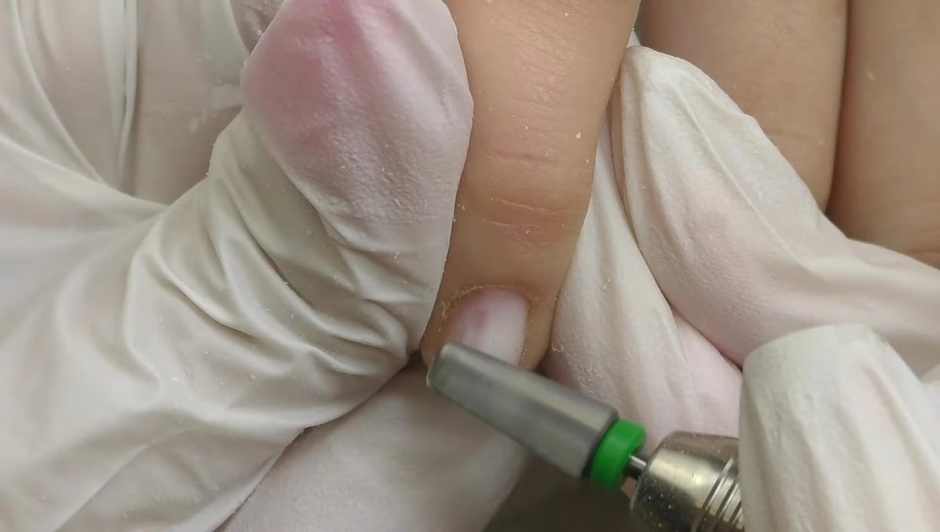 Close-up of the nail drill removing gel polish from a short nail.