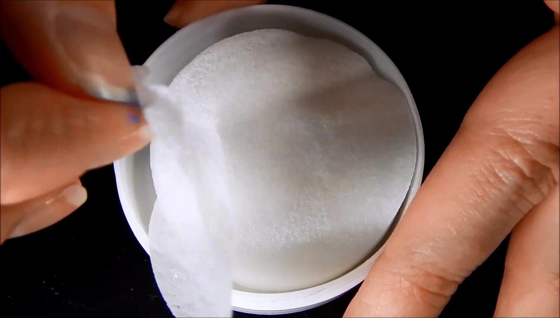 A hand holding one of the thin and flimsy nail polish remover pads.