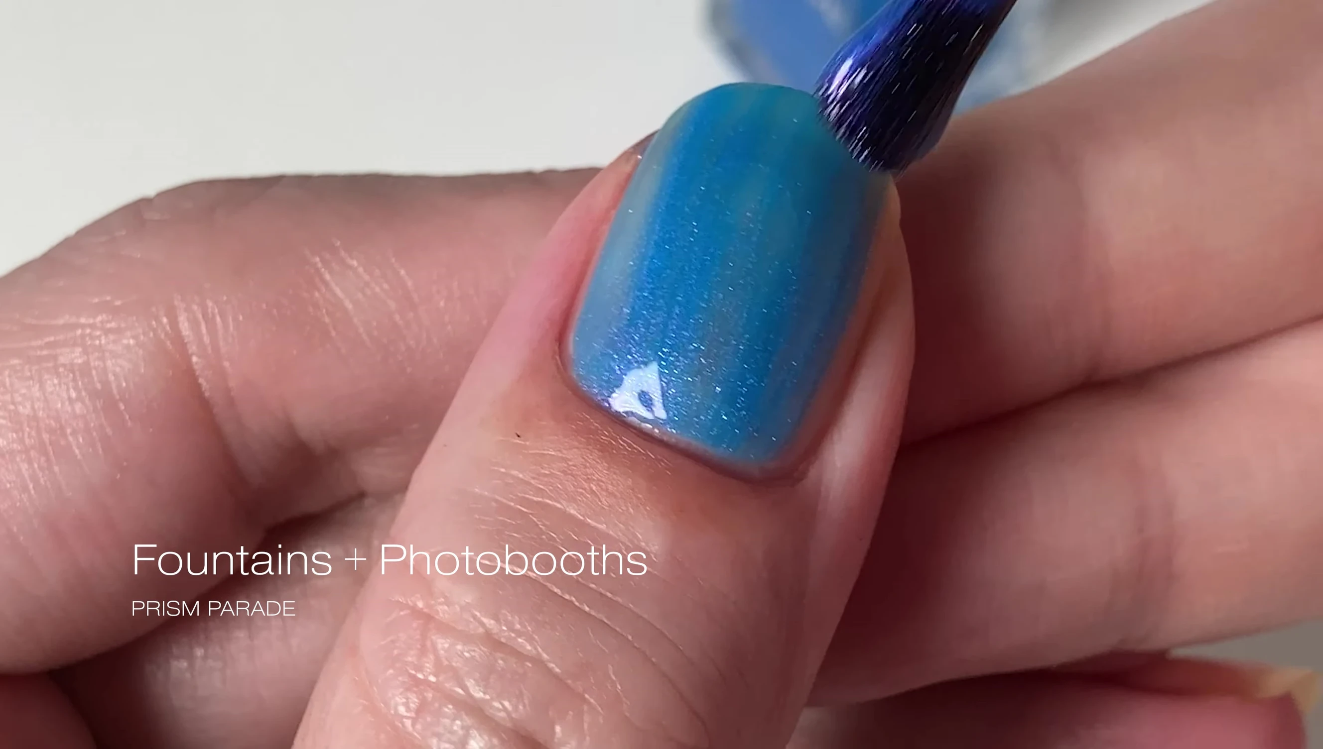 Close-up of Fountains and Photo Booths nail polish on a finger, highlighting the blue color and pinkish-purple shimmer.
