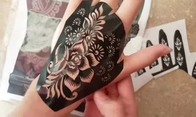 Person using a brush to fill in gaps with henna paste around the sticker.